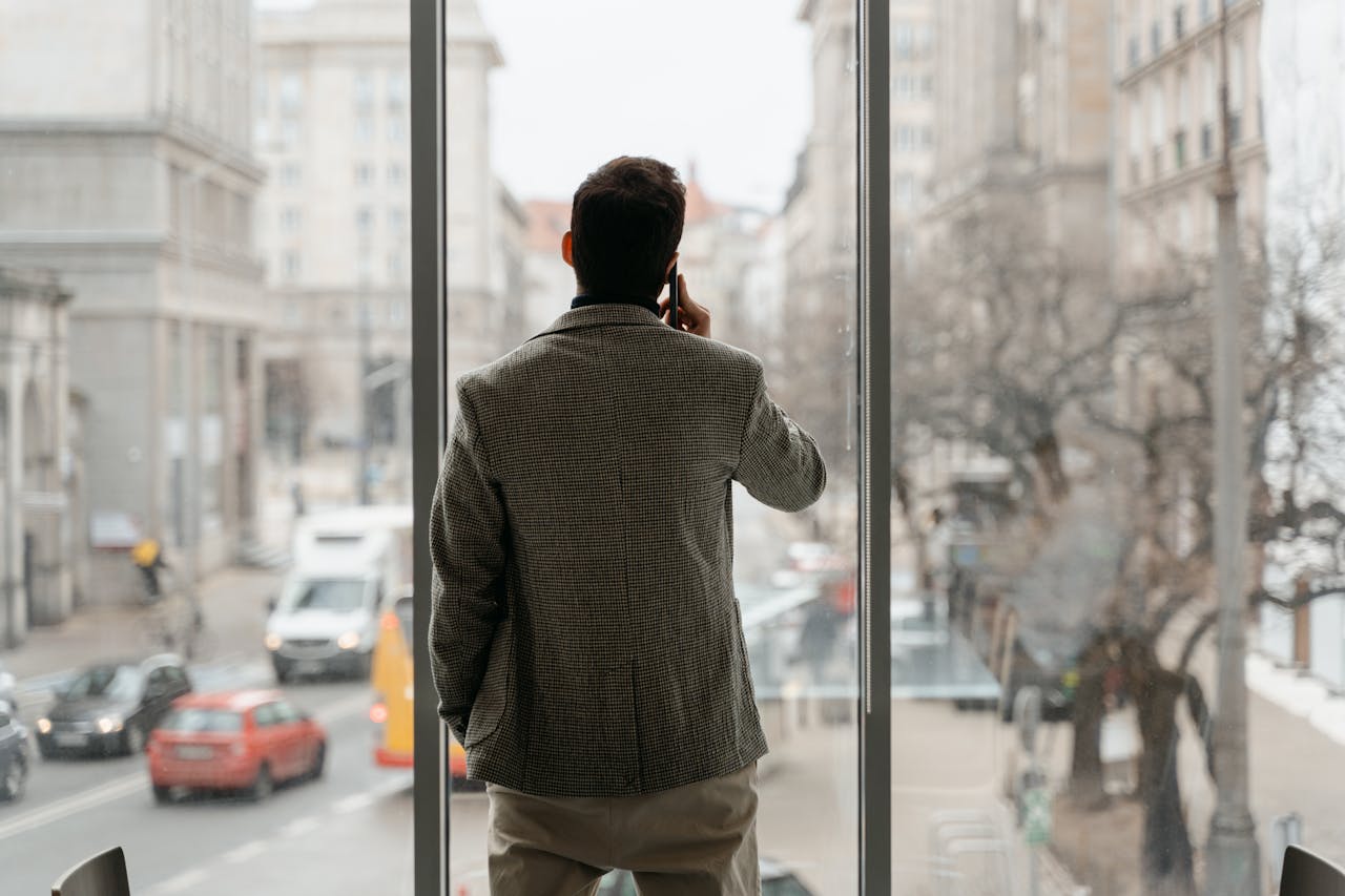 our-services-1 A businessman on a phone call, standing next to a window overlooking a busy city street.